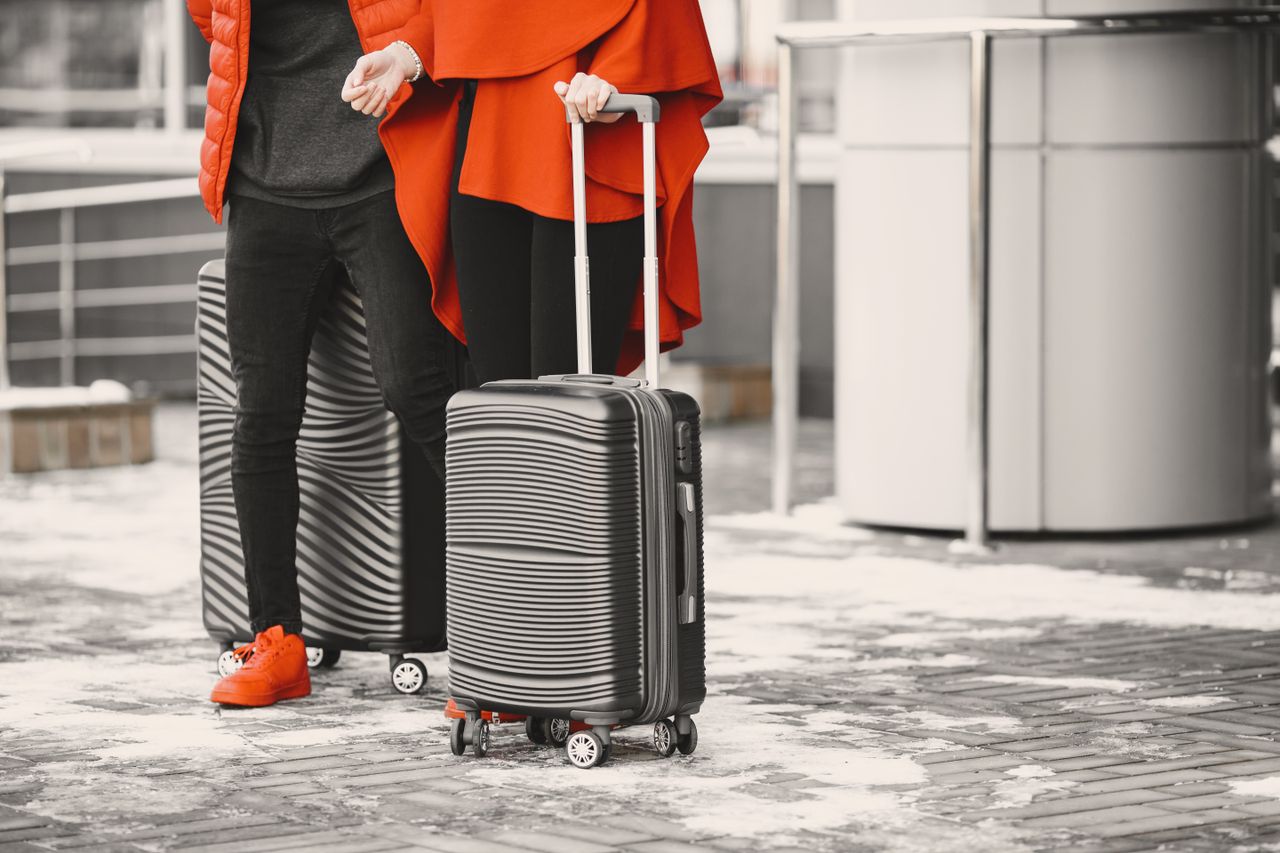 A fashionable couple in winter attire with sleek luggage, standing outdoors on a snowy day.